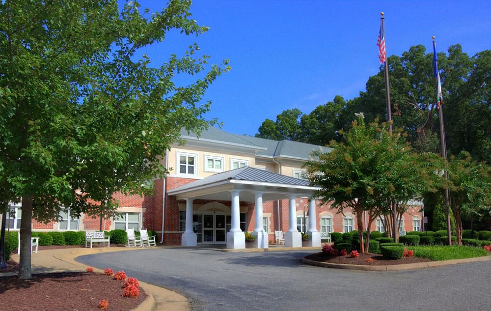 Front entrance of Charter Senior Living of Williamsburg, VA with manicured landscaping and American flags